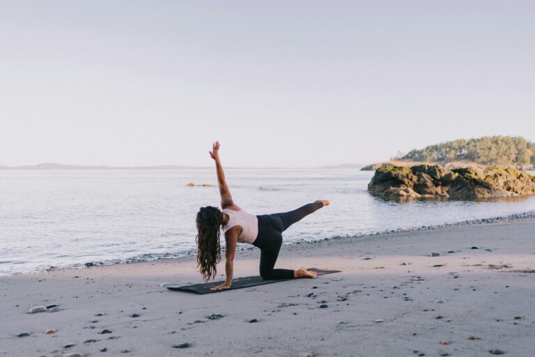 Woman practicing spiritual yoga pose on serene beach at sunset, demonstrating mindful exercise and meditation by ocean waves